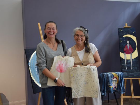 Prowadząca warsztaty i uczestniczka prezentują ręcznie malowane torby z motywami mandali i kwiatu.