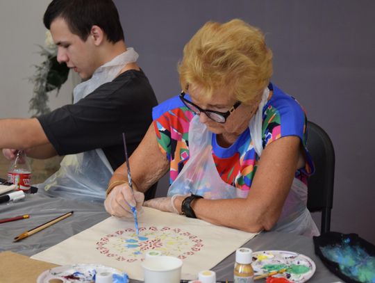Uczestniczka maluje mandalę na płóciennej torbie podczas warsztatów upcyklingu w Muzeum w Tomaszowie.