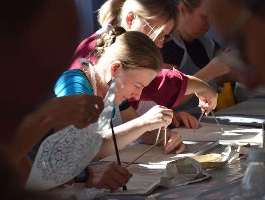 Zbliżenie: uczestniczki rysują mandale na tkaninie z użyciem szablonów i cyrkla.