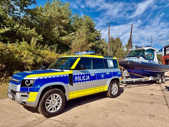 Land Rover Defender z przyczepą i łodzią policyjną – zestaw do działań w trudnym terenie.