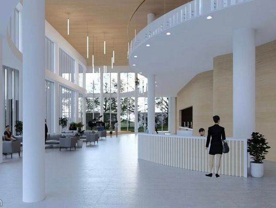 Przeszklone foyer za dnia z widokiem na zieleń, lady recepcyjnej i wiszących opraw świetlnych.