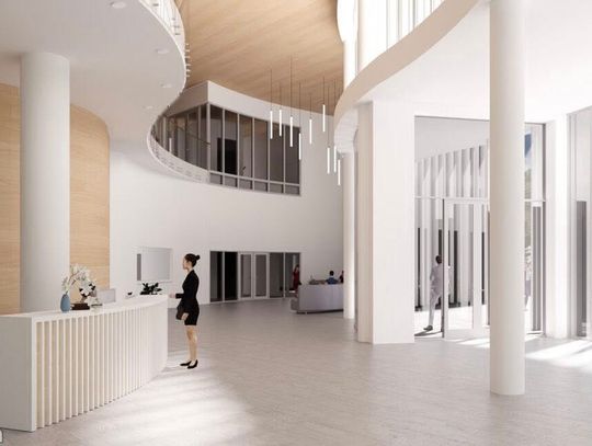 Recepcja przy filarze, jasne ściany i wysokie przeszklenia przy wejściu do budynku.