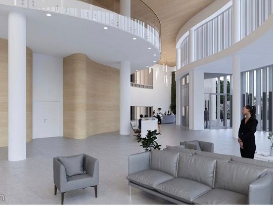 Przestrzeń foyer z rytmem białych słupów i dużymi oknami, strefy wypoczynku po lewej.