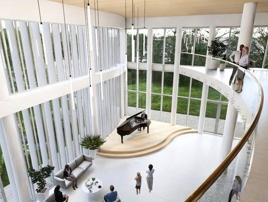 Widok z górnej galerii na zieloną ścianę i strefę siedzącą w holu, pionowe lampy zawieszone nad przestrzenią.