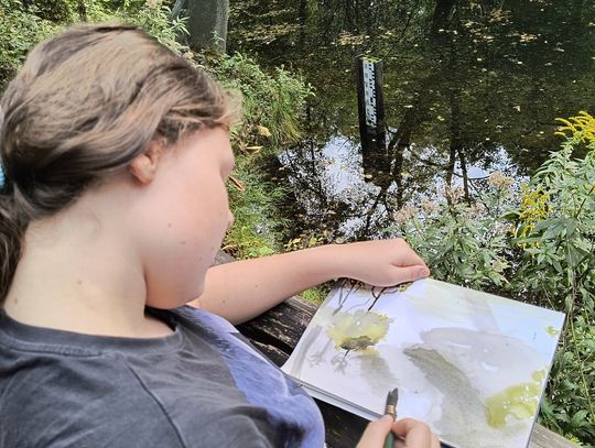 Plener malarski w sercu rezerwatu Uczennica szkicuje pejzaż nad wodą w rezerwacie Niebieskie Źródła – połączenie sztuki i biologii