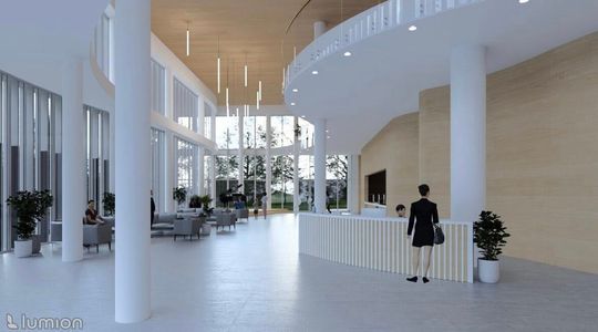 Przeszklone foyer za dnia z widokiem na zieleń, lady recepcyjnej i wiszących opraw świetlnych.