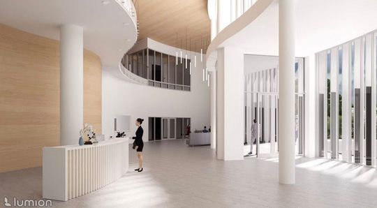 Recepcja przy filarze, jasne ściany i wysokie przeszklenia przy wejściu do budynku.