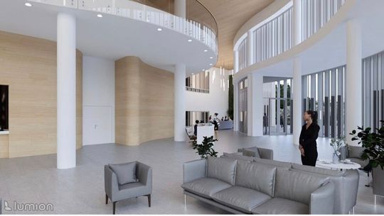 Przestrzeń foyer z rytmem białych słupów i dużymi oknami, strefy wypoczynku po lewej.