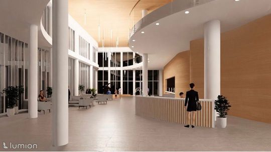 Jasne foyer sali koncertowej z recepcją, wysokim sufitem z drewnem i pionowymi lampami, widoczne przeszklenia i strefa siedząca.