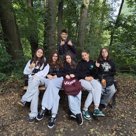 Grupa uczniów SP6 odpoczywa na ławce w cieniu drzew – relaks i regeneracja podczas zajęć terenowych