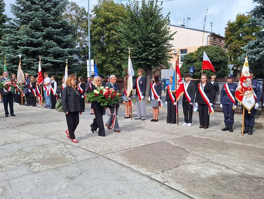 Kolumna delegacji z wieńcami idzie między pocztami sztandarowymi