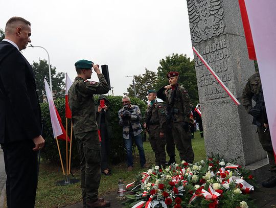 Żołnierze salutują przy pomniku z biało-czerwonymi wieńcami