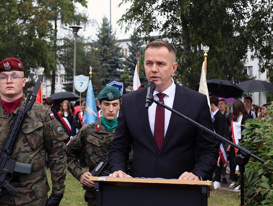 Wystąpienie przy mównicy, w tle żołnierze i poczty sztandarowe