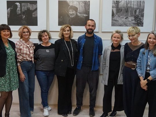 Grupowe zdjęcie organizatorów i gościa na tle czarno-białych prac podczas wystawy w Miejskiej Bibliotece Publicznej w Tomaszowie Mazowieckim.