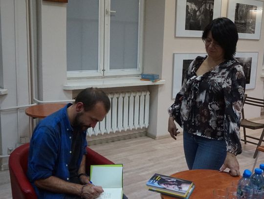 Autor składa podpis w egzemplarzu książki dla uczestniczki wydarzenia w czytelni Miejskiej Biblioteki Publicznej w Tomaszowie Mazowieckim.