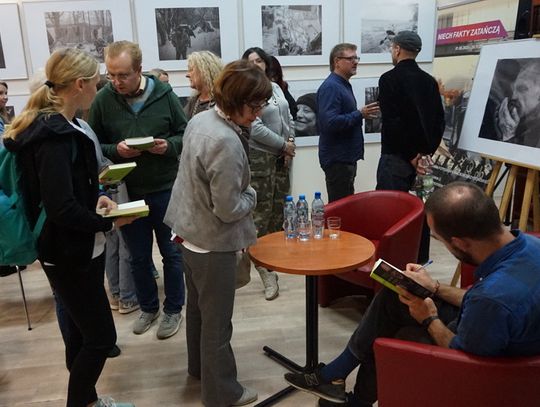 Czytelnicy z książkami ustawieni przy stoliku z autografami w czytelni MBP; na ścianach czarno-białe fotografie dokumentalne.