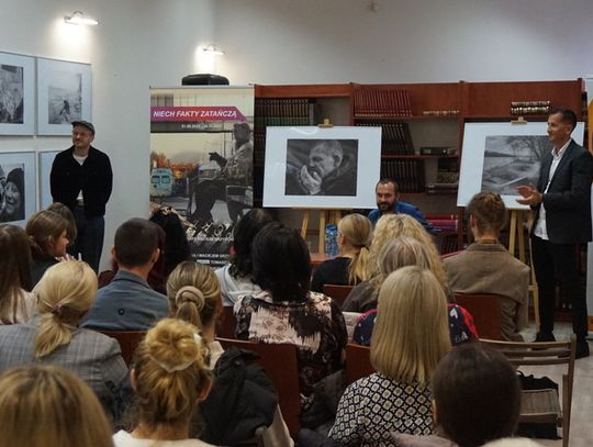Prelegenci przed publicznością; czarno-białe fotografie na sztalugach, banery MBP i „Niech fakty zatańczą” w czytelni.