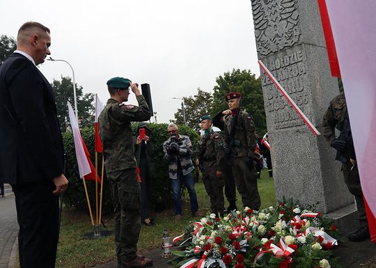 Żołnierze salutują przy pomniku z biało-czerwonymi wieńcami
