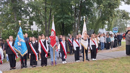 Uczniowie w szarfach trzymają sztandary szkolne podczas uroczystości