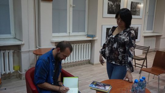 Autor składa podpis w egzemplarzu książki dla uczestniczki wydarzenia w czytelni Miejskiej Biblioteki Publicznej w Tomaszowie Mazowieckim.