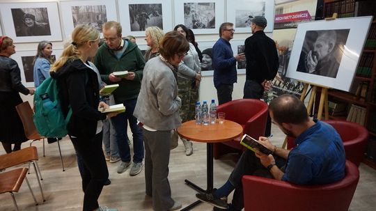 Czytelnicy z książkami ustawieni przy stoliku z autografami w czytelni MBP; na ścianach czarno-białe fotografie dokumentalne.