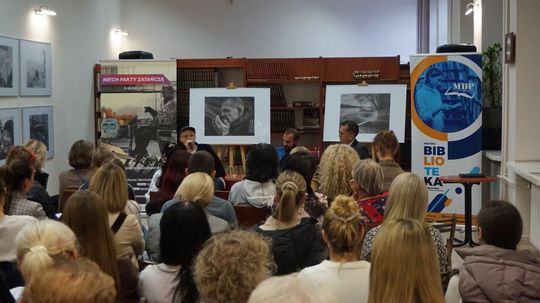 Widok sali od tyłu; panel z rozmówcami, banery MBP i „Niech fakty zatańczą”, fotografie na sztalugach.