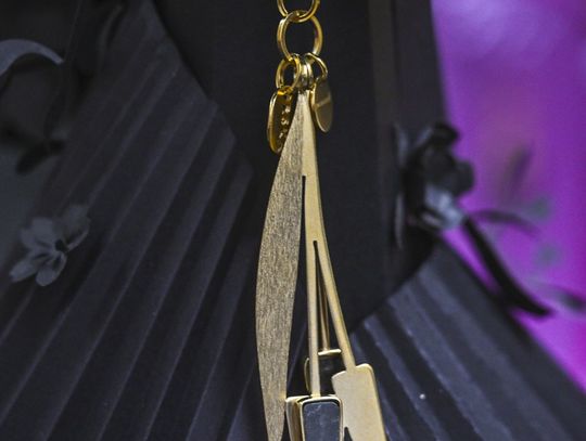 Zbliżenie na pozłacany brelok z elementem ceramicznym, zawieszony na czarnym tle.