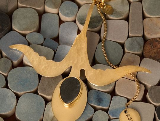 Pozłacany brelok z elementem ceramicznym ułożony na mozaice płytek.