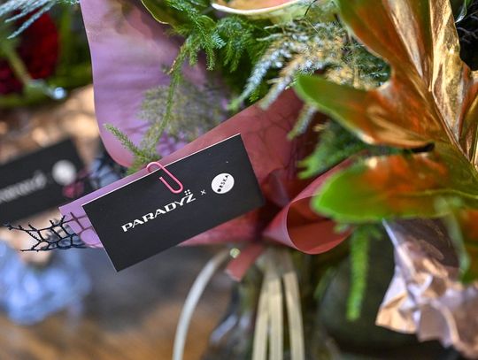 Zbliżenie na kartę z logo PARADYŻ x ORSKA przypiętą do kwiatów.