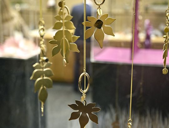 Zbliżenie na pozłacane zawieszki w kształcie liści na cienkich łańcuszkach w gablocie.
