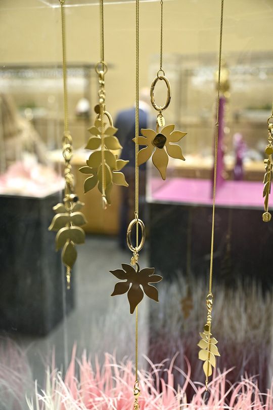 Zbliżenie na pozłacane zawieszki w kształcie liści na cienkich łańcuszkach w gablocie.