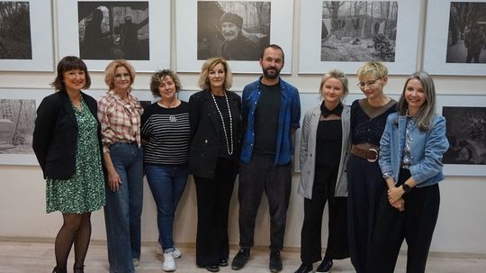 Grupowe zdjęcie organizatorów i gościa na tle czarno-białych prac podczas wystawy w Miejskiej Bibliotece Publicznej w Tomaszowie Mazowieckim.