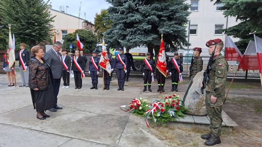 Złożenie kwiatów pod miejscem pamięci Sybiraków Delegacja składa wieniec przy kamiennym obelisku, asysta wojskowa w szyku
