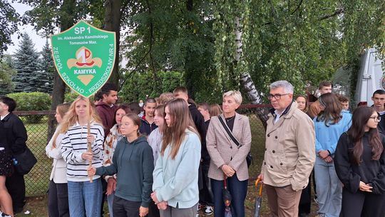 SP1 „Kamyka” na obchodach 17 września Uczniowie SP1 z tablicą szkoły stoją pod drzewami podczas uroczystości