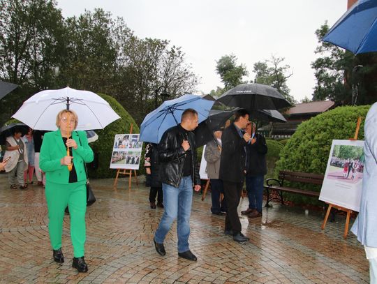 Grupa osób przechadza się z parasolami obok plansz z historią Dożynek w Spale.