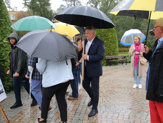 Ludzie pod parasolami rozmawiają, oglądając ekspozycję o dożynkach w spalskim parku.