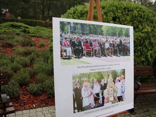 Tablica z archiwalnymi zdjęciami Dożynek Prezydenckich 2005 ustawiona na sztaludze w parku.