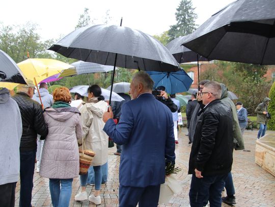 Uczestnicy wydarzenia w Spale idą alejką z parasolami podczas deszczu.