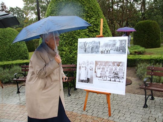 Kobieta z parasolem ogląda planszę z archiwalnymi zdjęciami dożynek na wystawie w parku w Spale.