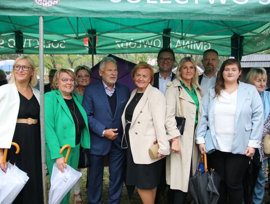 Duża grupa uśmiechniętych osób pozuje pod namiotem podczas deszczu.