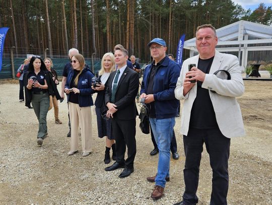 Niewiadów: uczestnicy ogłoszenia partnerstwa Grupa osób stoi na żwirowym placu przy lesie podczas wydarzenia branżowego; w tle namiot i banery.