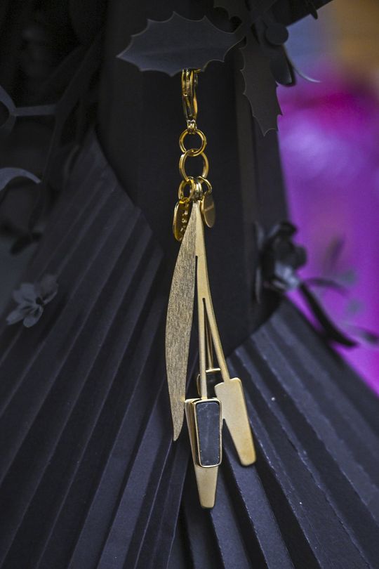 Detal kolekcji – pozłacany brelok ORSKA x PARADYŻ Zbliżenie na pozłacany brelok z elementem ceramicznym, zawieszony na czarnym tle.