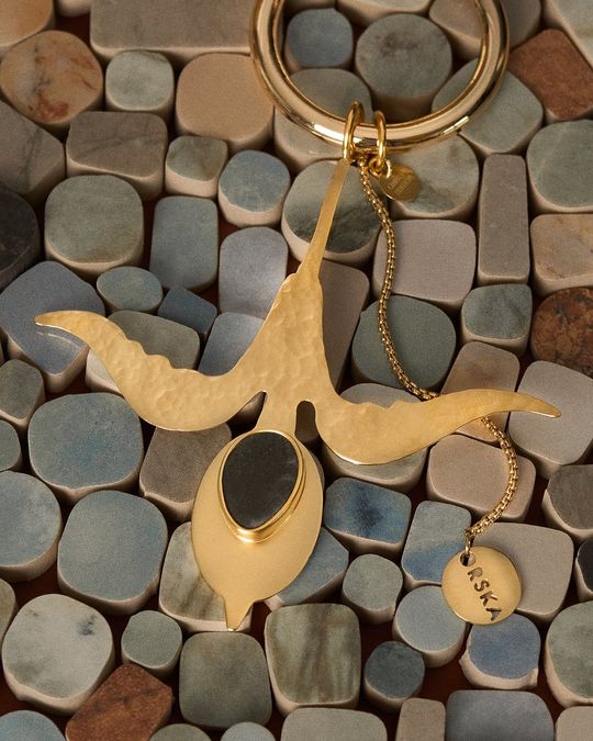 Produkt – brelok ORSKA x PARADYŻ na tle ceramiki Pozłacany brelok z elementem ceramicznym ułożony na mozaice płytek.