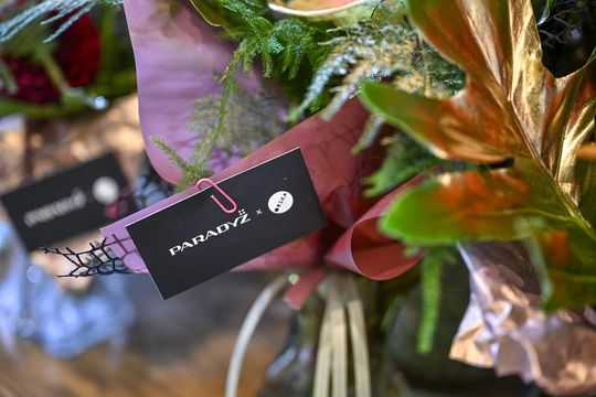 Branding wydarzenia – PARADYŻ x ORSKA na bukietach Zbliżenie na kartę z logo PARADYŻ x ORSKA przypiętą do kwiatów.