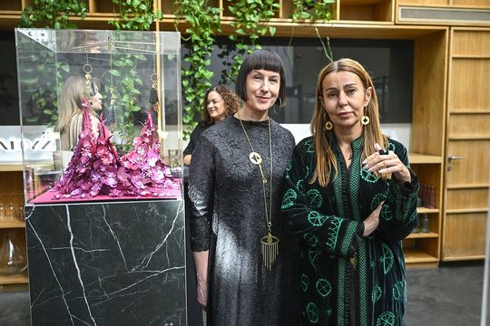 Przy fuksjowej gablocie – projekt i premiera Dwie uczestniczki stoją obok gabloty z różowo-fuksjową instalacją i pozłacanymi brelokami.