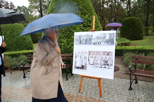 Kobieta z parasolem ogląda planszę z archiwalnymi zdjęciami dożynek na wystawie w parku w Spale.