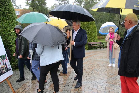 Deszczowe rozmowy między planszami Ludzie pod parasolami rozmawiają, oglądając ekspozycję o dożynkach w spalskim parku.