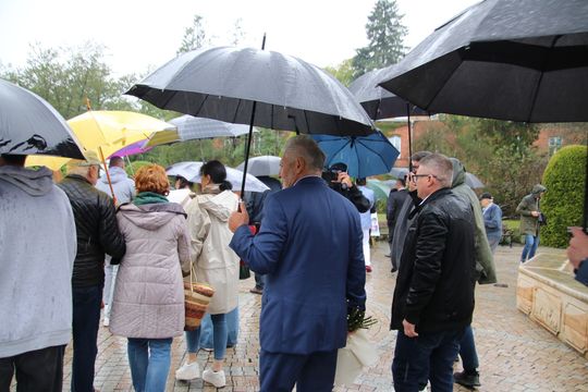 Uczestnicy uroczystości pod parasolami Uczestnicy wydarzenia w Spale idą alejką z parasolami podczas deszczu.