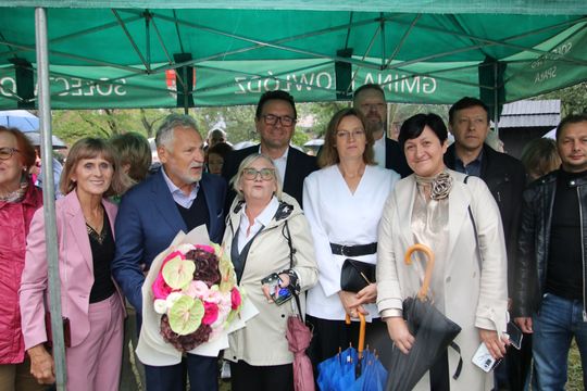 Pamiątkowe zdjęcie z gośćmi wydarzenia Grupa uczestników pozuje pod zielonym namiotem, w centrum bukiet kwiatów.