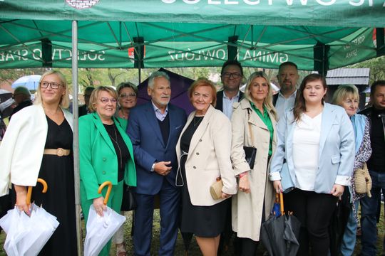 Wspólna fotografia uczestników pod namiotem Duża grupa uśmiechniętych osób pozuje pod namiotem podczas deszczu.